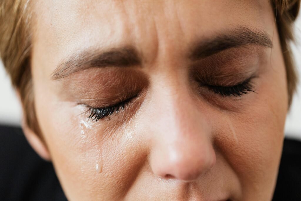 Emotional close-up of a woman's face with closed eyes and tears expressing distress.