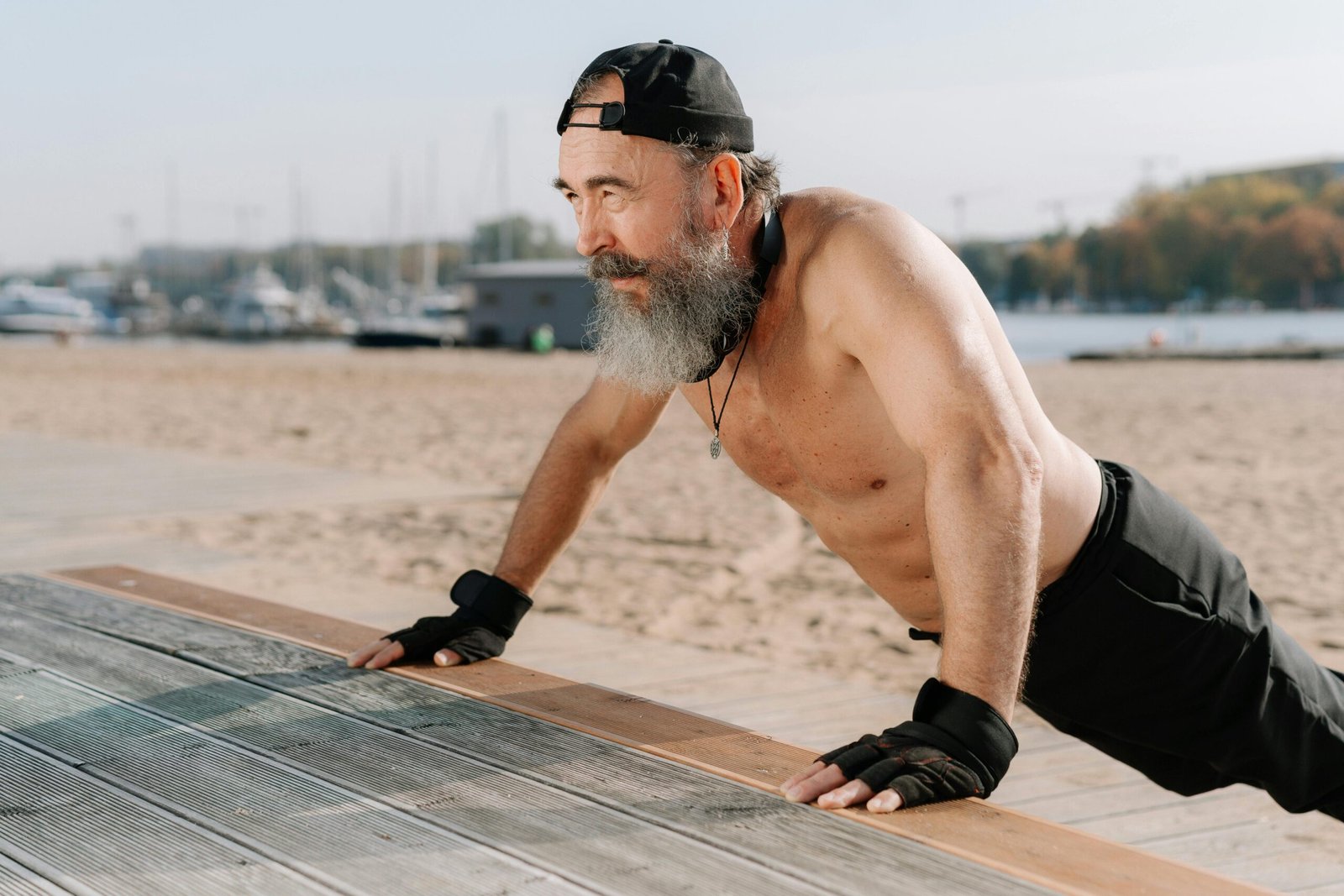 Fit senior man doing push ups on a sunny beach day promoting healthy lifestyle.