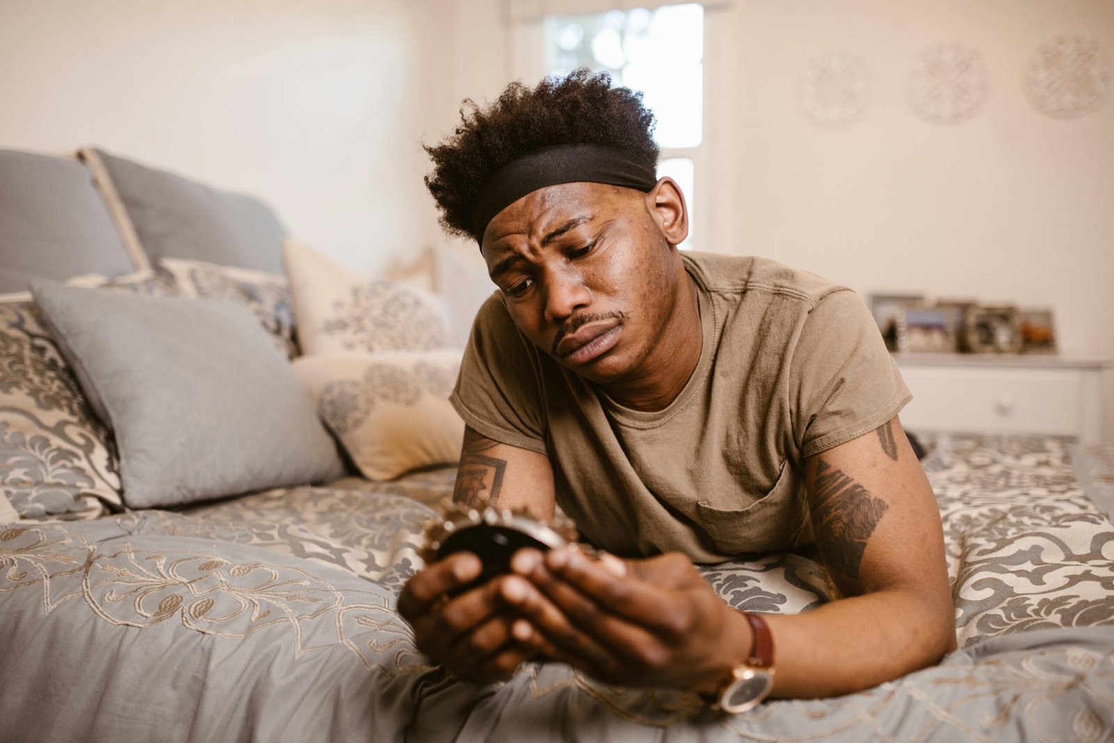 A man lies on a bed, looking pensively at a picture frame, conveying emotion.