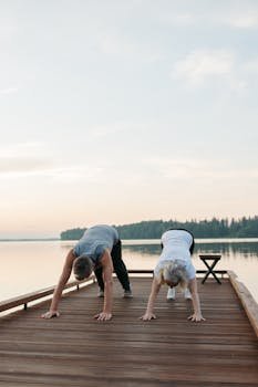 pexels-photo-8795593-8795593 50's couple practicing outdoor yoga on a wooden dock by a serene lake at sunset, promoting fitness and mindfulness.